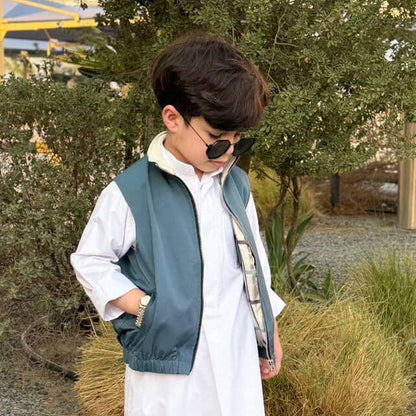 Child wearing a long white coat, blue vest, and sunglasses outdoors.